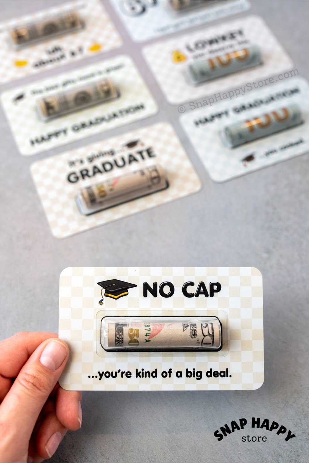fp:50% 80% | Graduation-themed greeting card with humorous no cap text held by a hand on a gray background